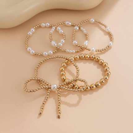 Gold multi-layer stretch bracelet featuring pearl beads, ball chain details, and a bow charm styled on a wrist.