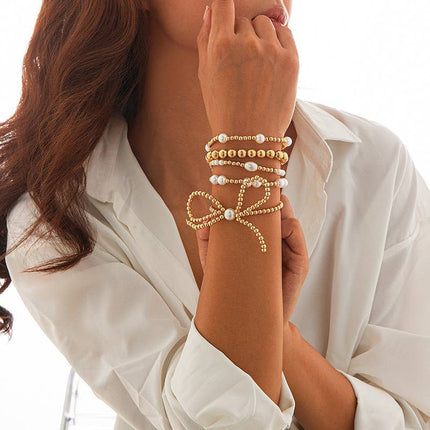 Gold multi-layer stretch bracelet featuring pearl beads, ball chain details, and a bow charm styled on a wrist.