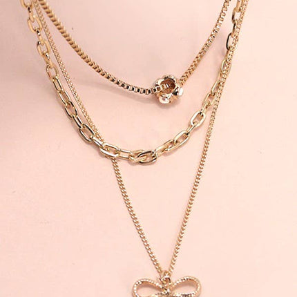 Layered gold necklace featuring delicate pearl strands and a small bow charm resting on a soft neutral background.
