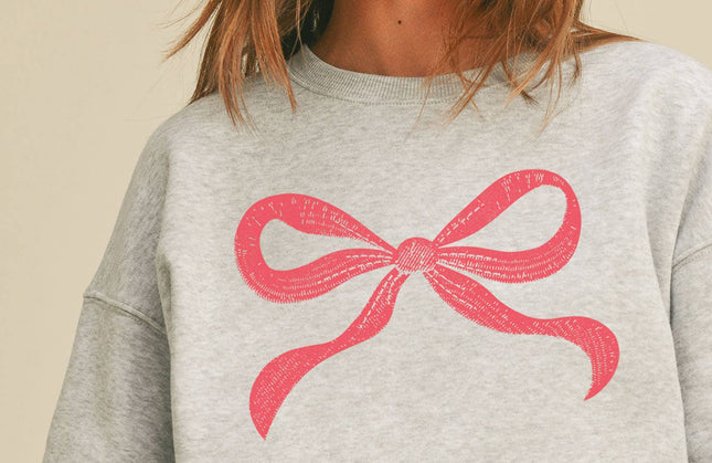 Light grey sweatshirt with pink bow graphic on chest, relaxed fit, drop shoulders, and ribbed hem and cuffs.