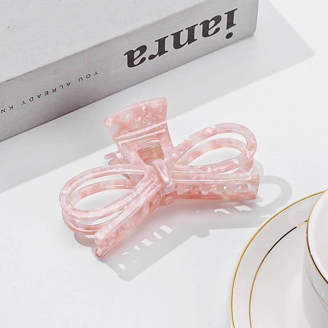 Pink bow-shaped hair clip on a white surface with 'ianra' branding in the background.