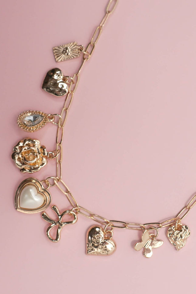 Gold charm bracelet with various charms on a pink background