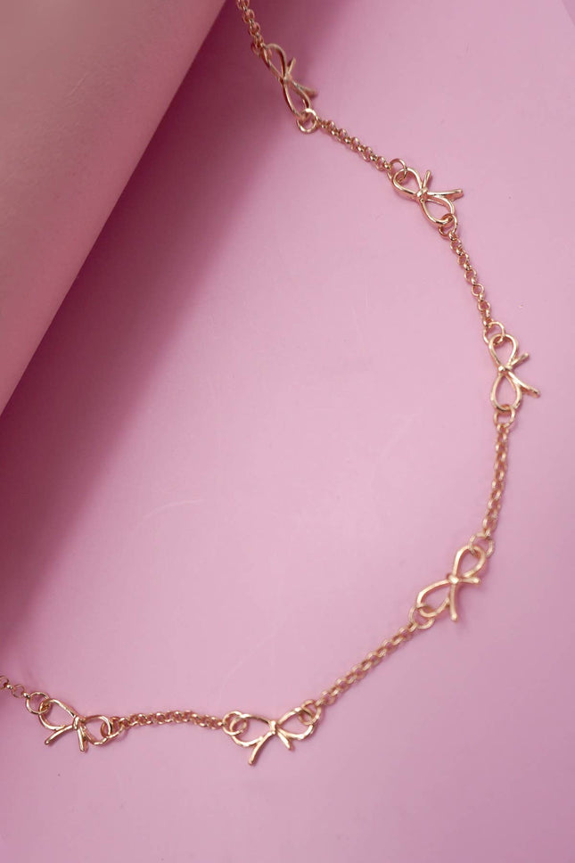 Gold-plated bow charm necklace with dainty cut-out ribbon stations and adjustable extender chain.