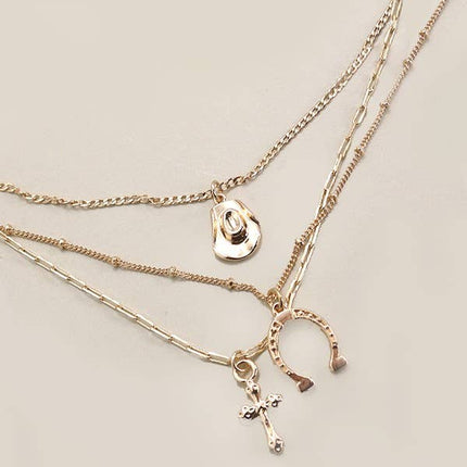 Gold plated multi-layer western inspired charm necklace with dangling horseshoe, porcelain hat and cross charms 