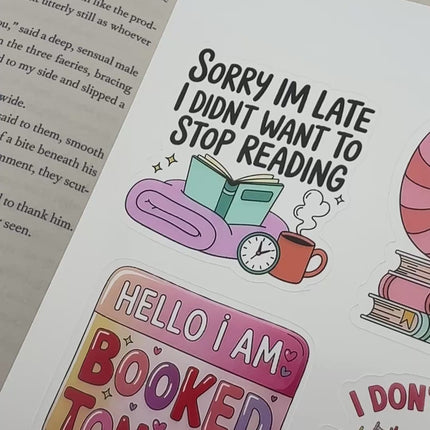 Multiple book lover sticker sheet designs featuring cozy reading themes, spicy book humor, hearts, books, and playful illustrations displayed on an open book background.