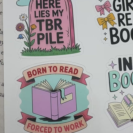 Multiple book lover sticker sheet designs featuring cozy reading themes, spicy book humor, hearts, books, and playful illustrations displayed on an open book background.