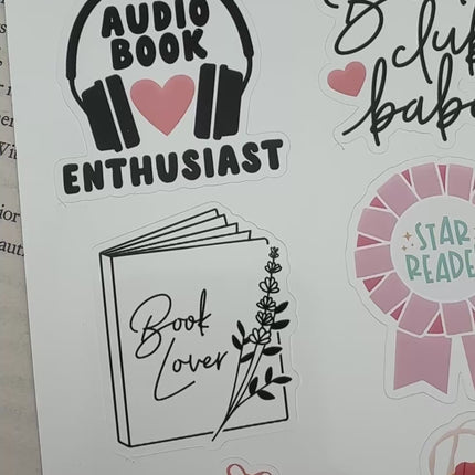 Multiple book lover sticker sheet designs featuring cozy reading themes, spicy book humor, hearts, books, and playful illustrations displayed on an open book background.
